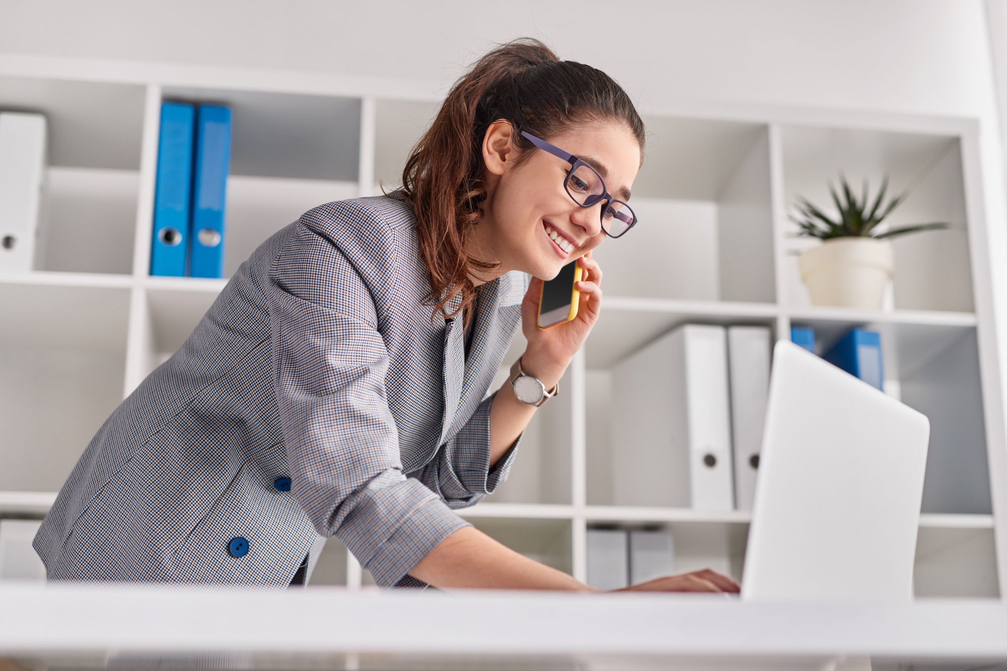 Cheerful secretary answering call and using laptop